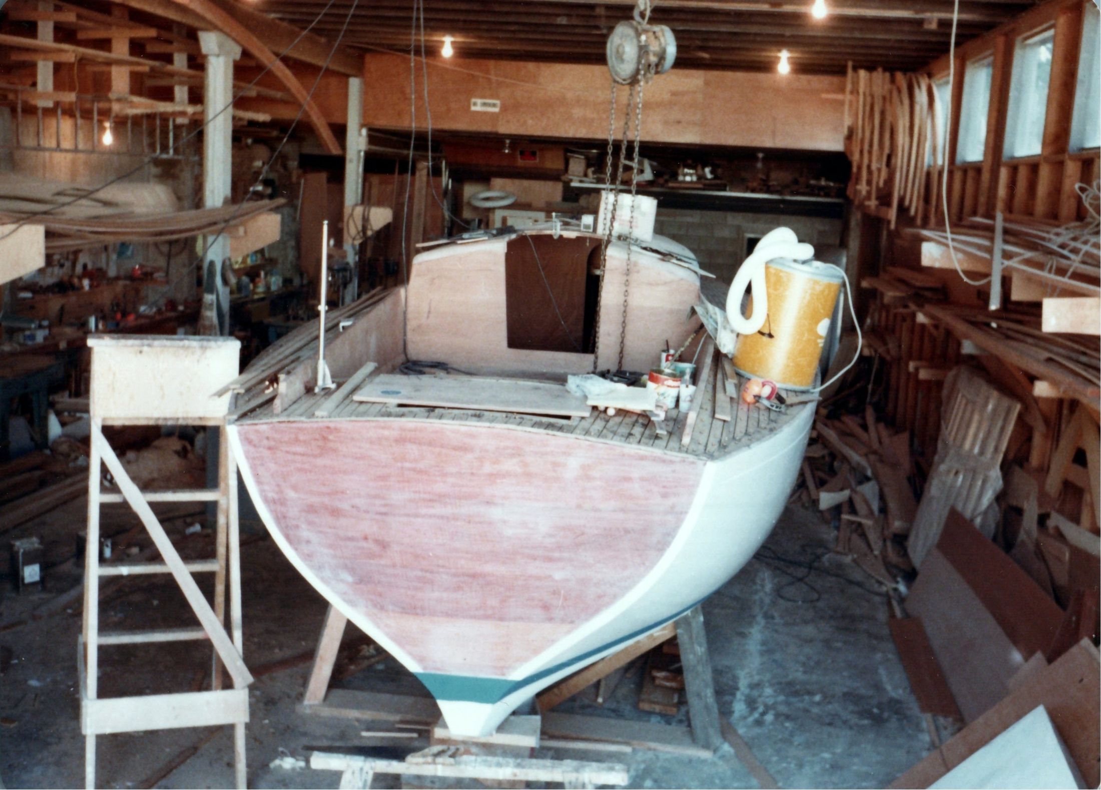 The boat in the shop with cabin and cockpit complete, a stepladder at the bow
