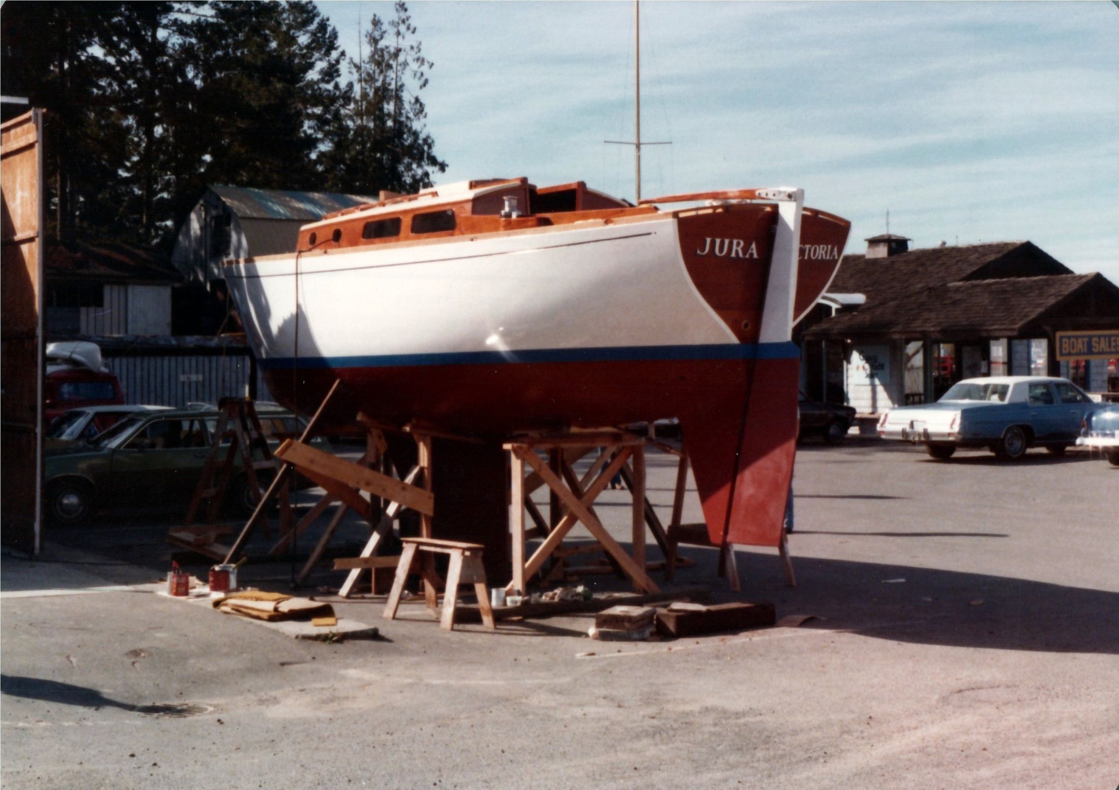 The boat on cradles, JURA on the transom, a car passing