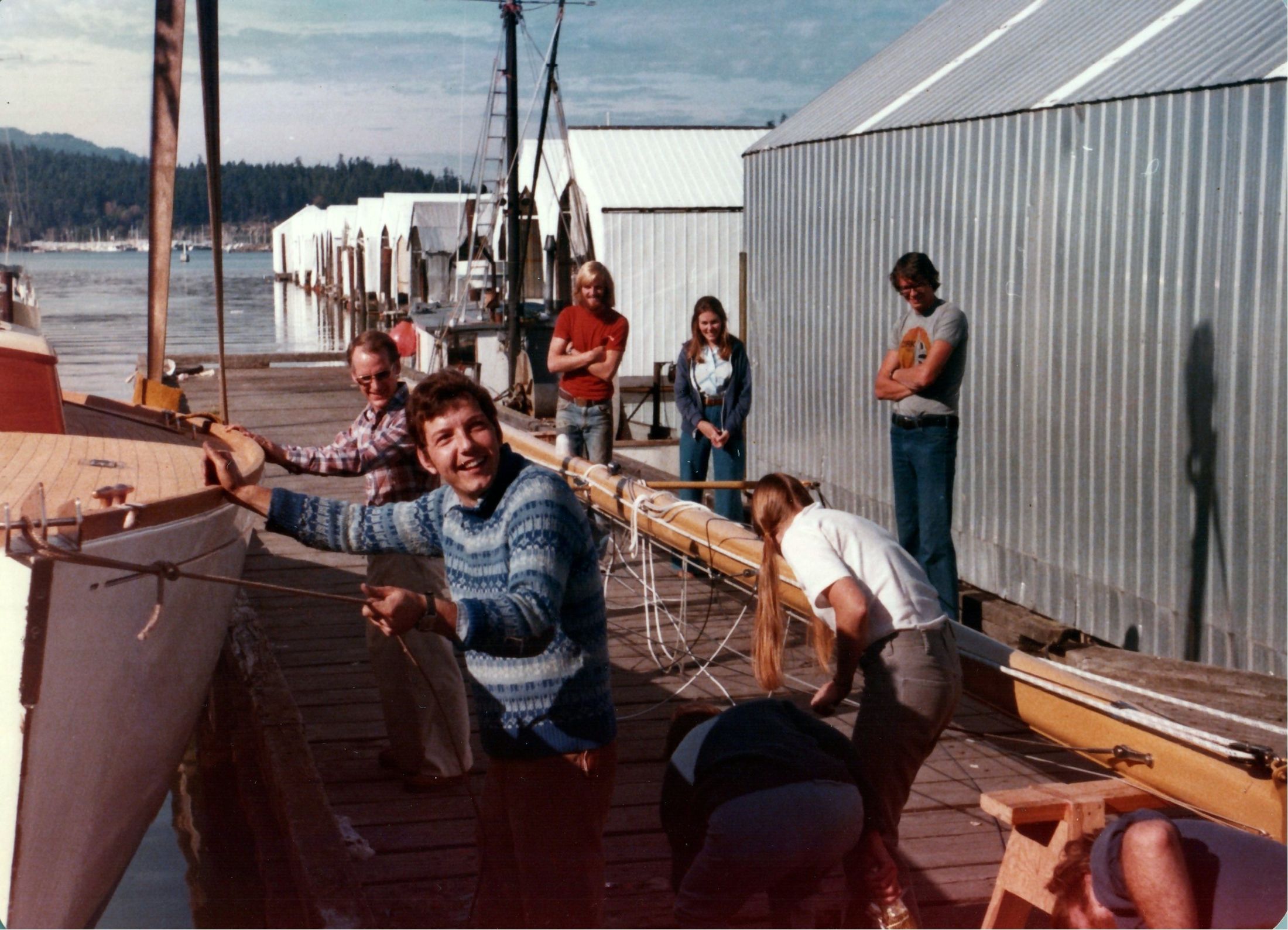 A man in a blue sweater laughing on the dock beside the bow